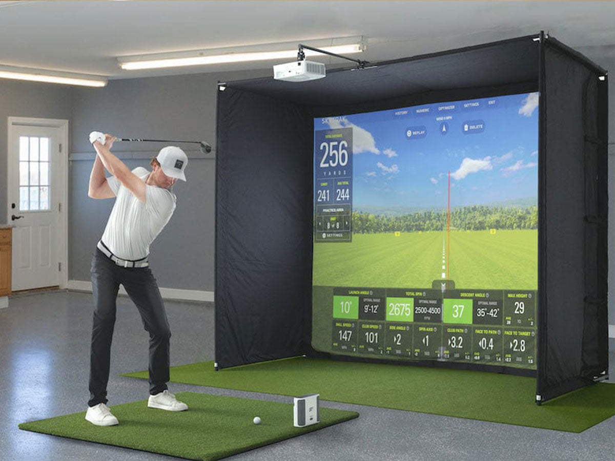 Person using a golf simulator in a home setting with a screen displaying a golf course.