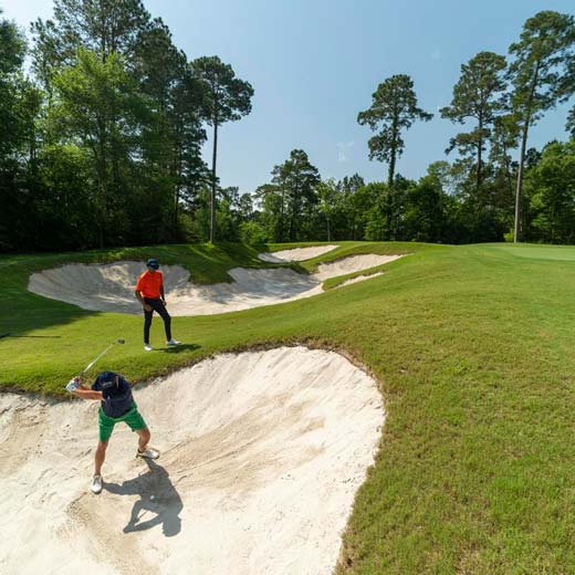 Man hitting a bunker shot with GOLFTEC coach watching over