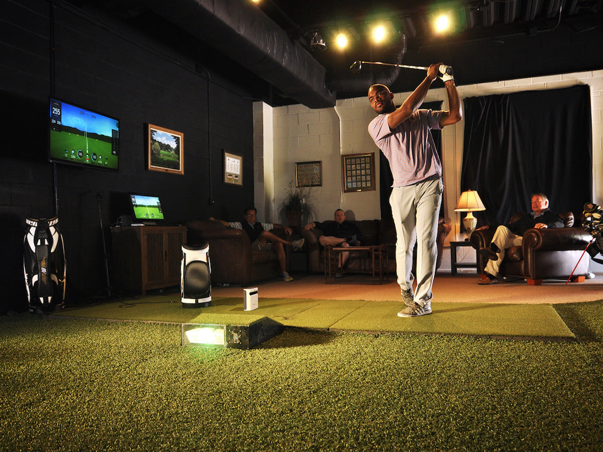 Man swinging a golf club with the SKYTRAK Protective Floor Projector Mount in use, while friends watch